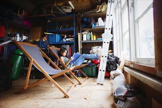 Mixed race girl reading in lawn chair in shed