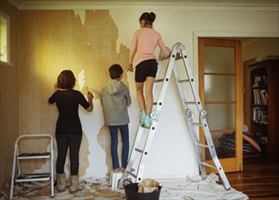 Mixed race mother and children stripping wallpaper in living room