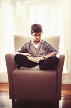 Mixed race boy reading book in armchair