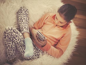 Mixed race girl using cell phone on in furry chair