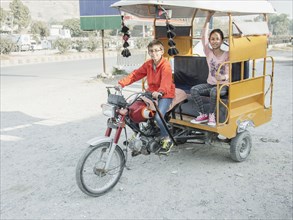 Mixed race boy driving girl in rickshaw
