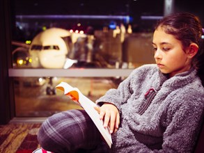 Mixed race girl reading book in airport