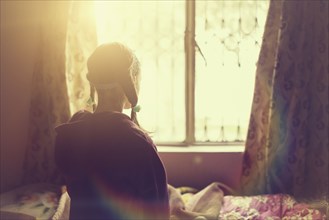 Mixed race girl looking out bedroom window