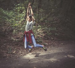 Mixed race girl swinging from tree branch on dirt path