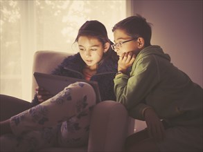 Mixed race children using digital tablet in living room