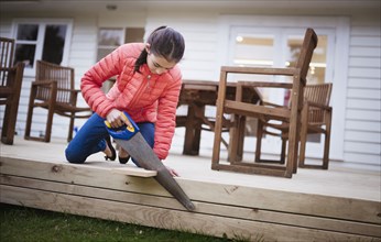 Mixed race girl sawing wood in backyard