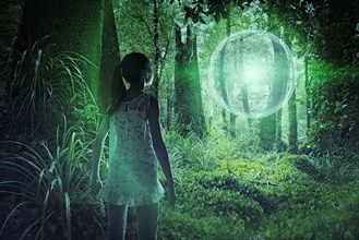 Mixed race girl discovering glowing sphere in forest