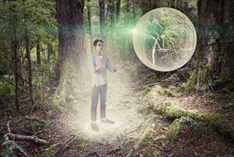 Mixed race boy admiring glowing orb in forest
