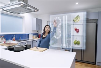 Mixed race woman using holographic screen in kitchen