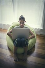 Mixed race girl using laptop in beanbag chair