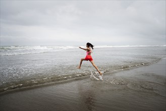 Mixed race girl running into ocean on beach