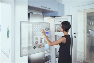 Mixed race girl using hologram refrigerator touch screen in kitchen