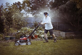 Caucasian man mowing lawn with VR goggles