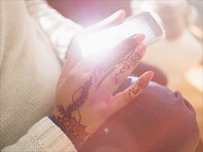 Woman with henna tattoos on hands texting on cell phone