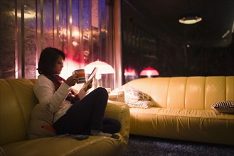 Woman drinking tea and reading magazine on sofa