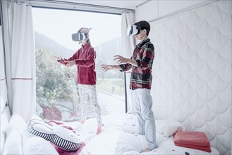 Mixed Race brother and sister using virtual reality goggles on bed