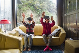 Mixed Race brother and sister using virtual reality goggles on sofa