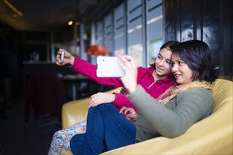 Mother and daughter sitting on sofa posing for cell phone selfie