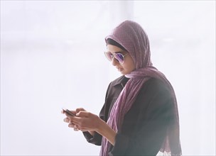 Mixed Race girl wearing heart-shape sunglasses and headscarf texting