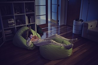 Mixed Race girl using cell phone laying on bean bags in dark
