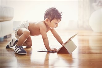 Indian baby boy crawling on floor with digital tablet