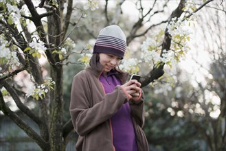 Smiling Mixed Race girl texting on cell phone near tree