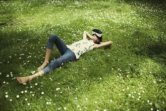 Mixed Race girl laying in grass wearing virtual reality goggles