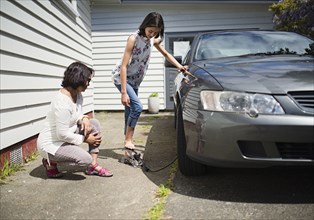 Mother watching daughter inflating car tire