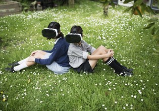 Mixed Race brother and sister sitting in grass wearing virtual reality goggles