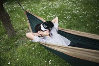 Mixed Race boy laying in hammock wearing virtual reality goggles