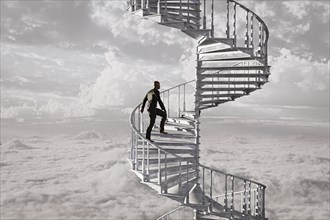 Man climbing spiral staircase in the clouds