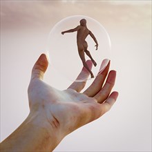 Hand holding naked man in sphere