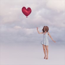 Girl releasing heart-shape balloon into sky