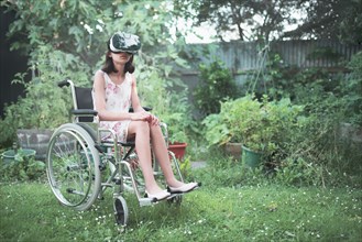 Mixed race girl in wheelchair using virtual reality goggles in backyard