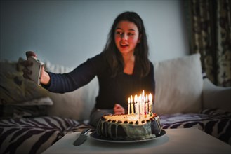 Mixed race girl posing for cell phone selfie with birthday cake