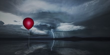 Red balloon floating in stormy sky