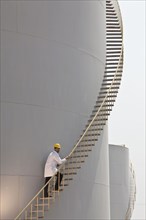 Caucasian worker climbing staircase on storage tank