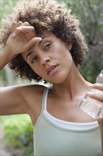 Mixed race woman wiping forehead and drinking water