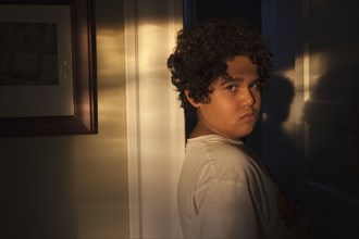 Unhappy mixed race boy in doorway with shadows
