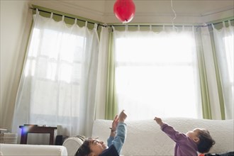 Mixed race children playing with balloon in living room