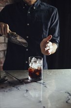 Caucasian bartender pouring ice in cocktail