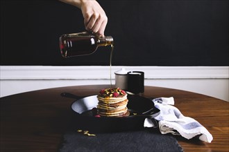Hand pouring syrup on pancakes