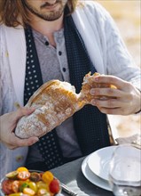 Caucasian man breaking bread at outdoor table