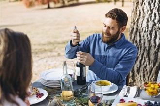 Caucasian man opening wine bottle at outdoor table