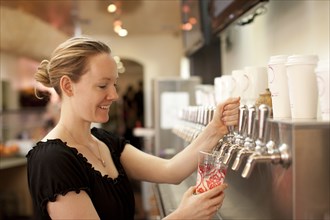 Smiling Caucasian woman filling cup from dispenser