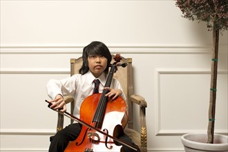 Vietnamese boy playing cello on elegant chair
