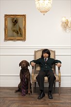 Vietnamese boy sitting on elegant chair next to dog with necktie