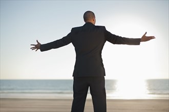 Mixed race businessman standing on beach with arms outstretched