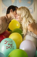 Caucasian couple kissing over balloon with 'save the date" text