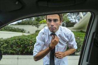 Hispanic businessman checking his tie in car door mirror